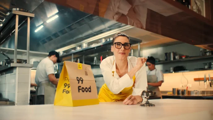 Cozinha com sacola de entrega amarela e equipe ao fundo.