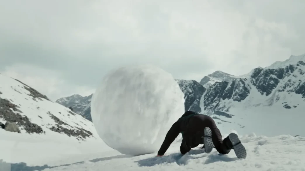 Pessoa empurrando bola de neve em montanha nevada.