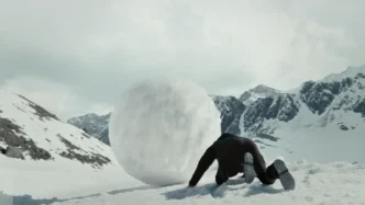 Pessoa empurrando bola de neve em montanha nevada.