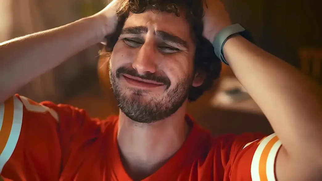 Homem frustrado com mãos na cabeça, camisa vermelha.