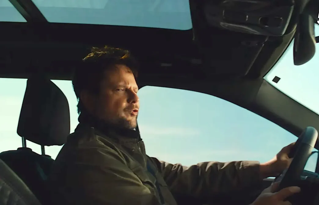 Homem dirigindo carro com teto solar aberto.