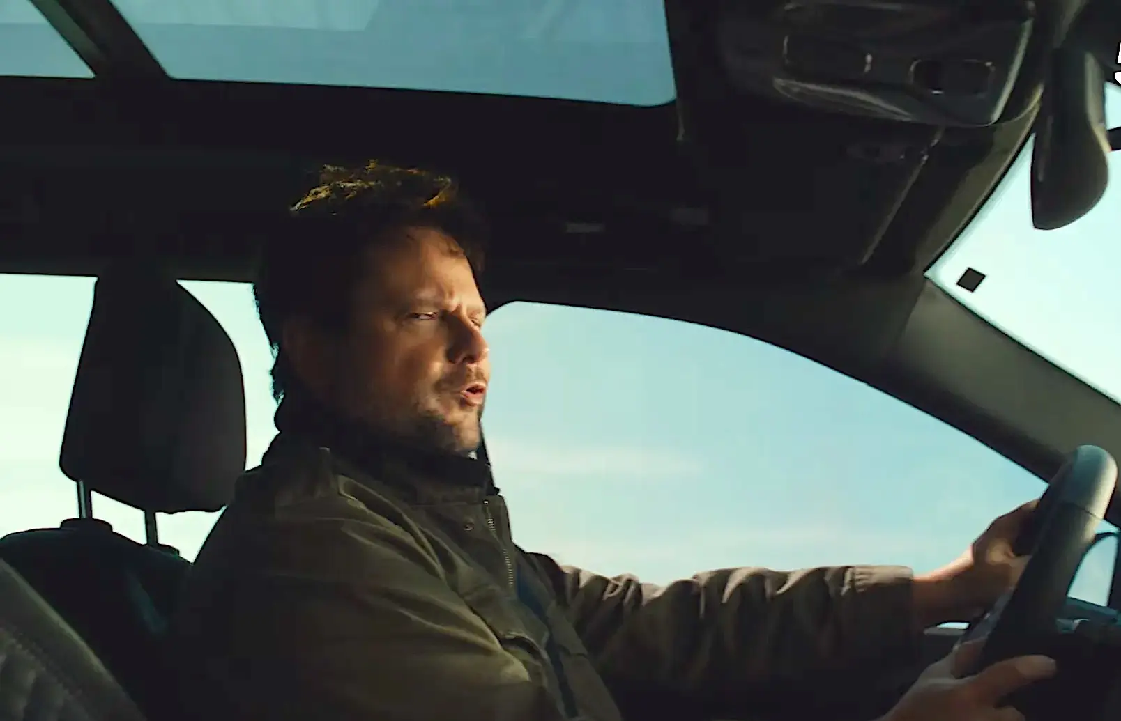 Homem dirigindo carro com teto solar aberto.