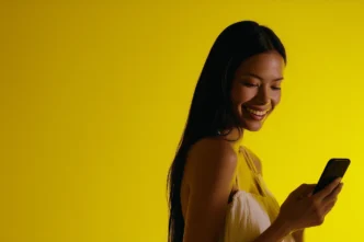 Mulher sorrindo olhando para o celular, fundo amarelo.