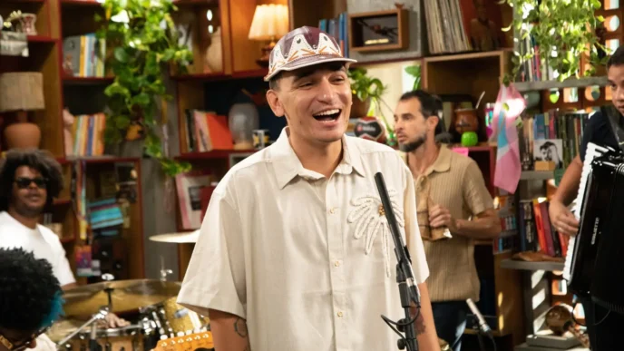 Homem sorrindo em estúdio com microfone e músicos.