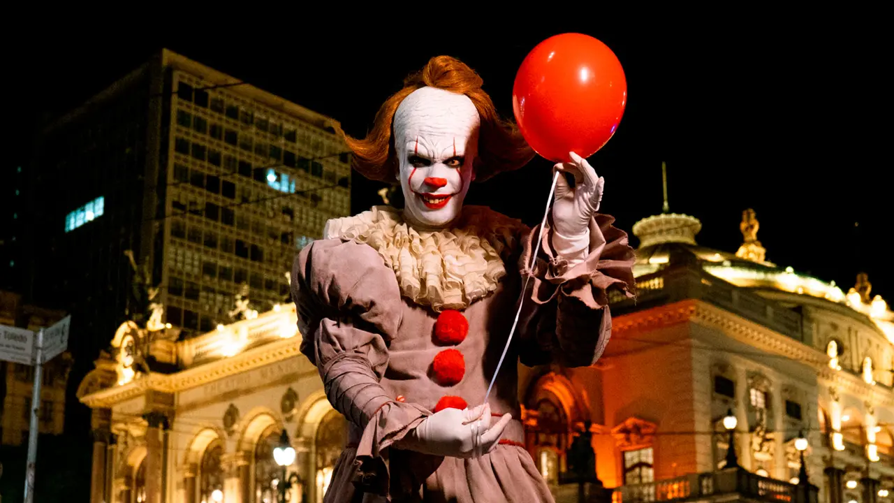 Palhaço segurando balão vermelho à noite.