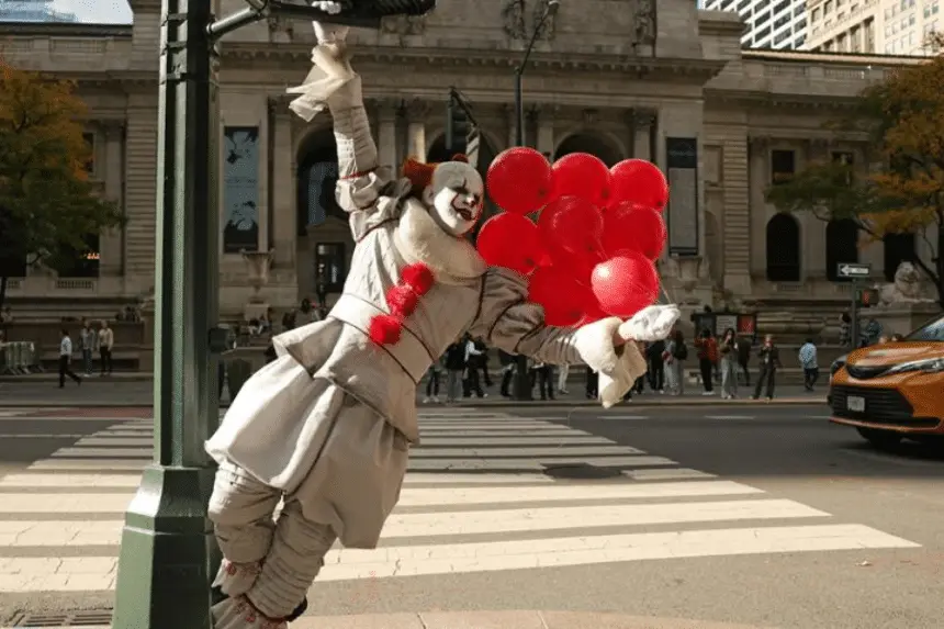 Palhaço segurando balões vermelhos na rua.