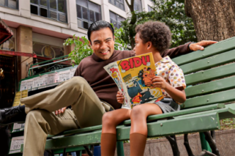 Homem e criança lendo gibi em banco de parque.