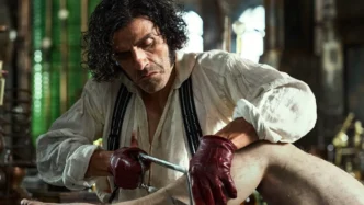 Homem serrando perna de manequim em cena sombria.