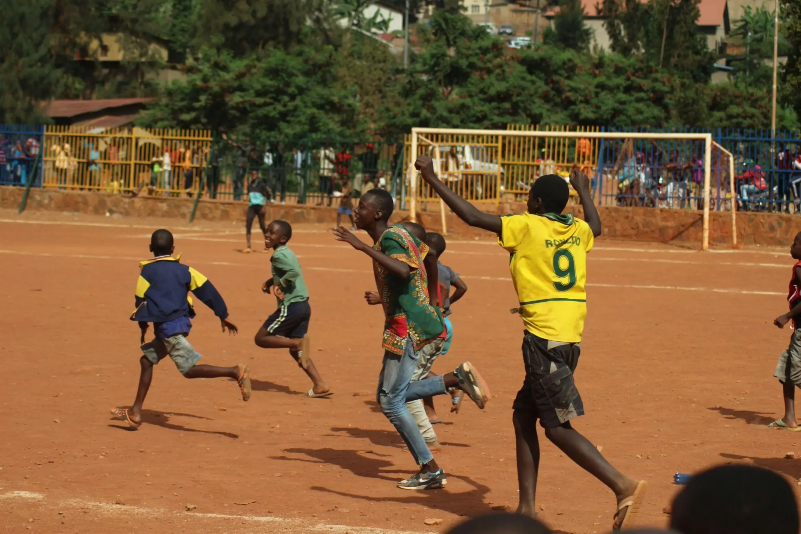 Crianças jogando futebol em campo de terra.
