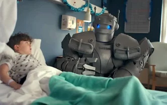 Criança deitada conversa com robô em hospital.