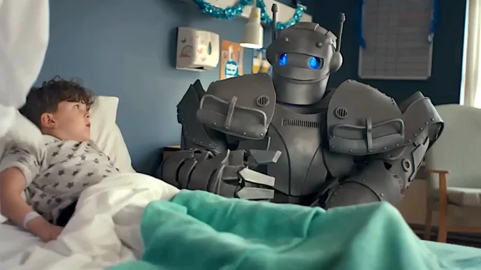 Criança deitada conversa com robô em hospital.