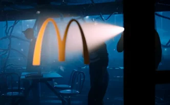 Logotipo McDonald's iluminado, interior escuro, pessoas ao fundo.