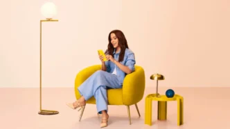 Pessoa sentada em poltrona, usando celular amarelo.