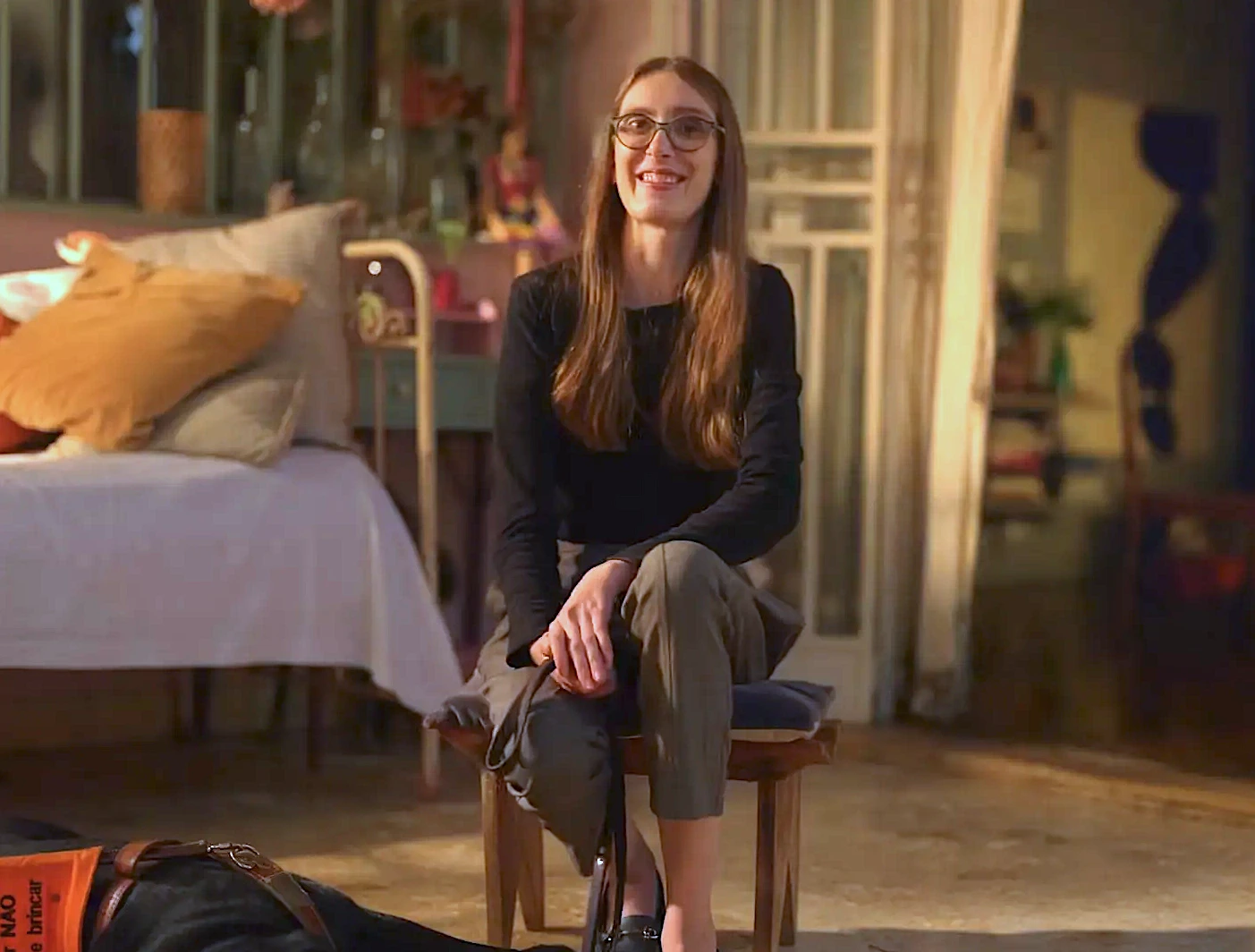 Mulher sorrindo sentada em cadeira, quarto aconchegante.