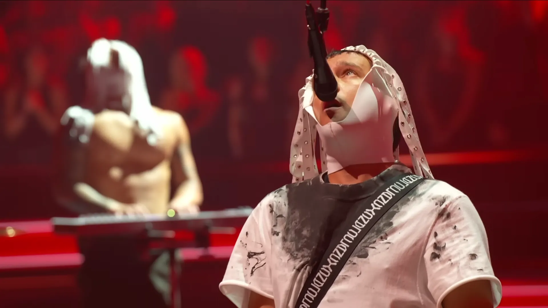 Performance artística com microfone e luzes vermelhas no palco.