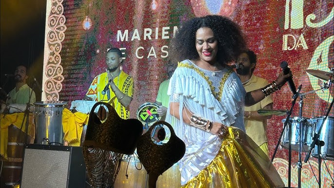 Cantora performa em palco com banda ao fundo.