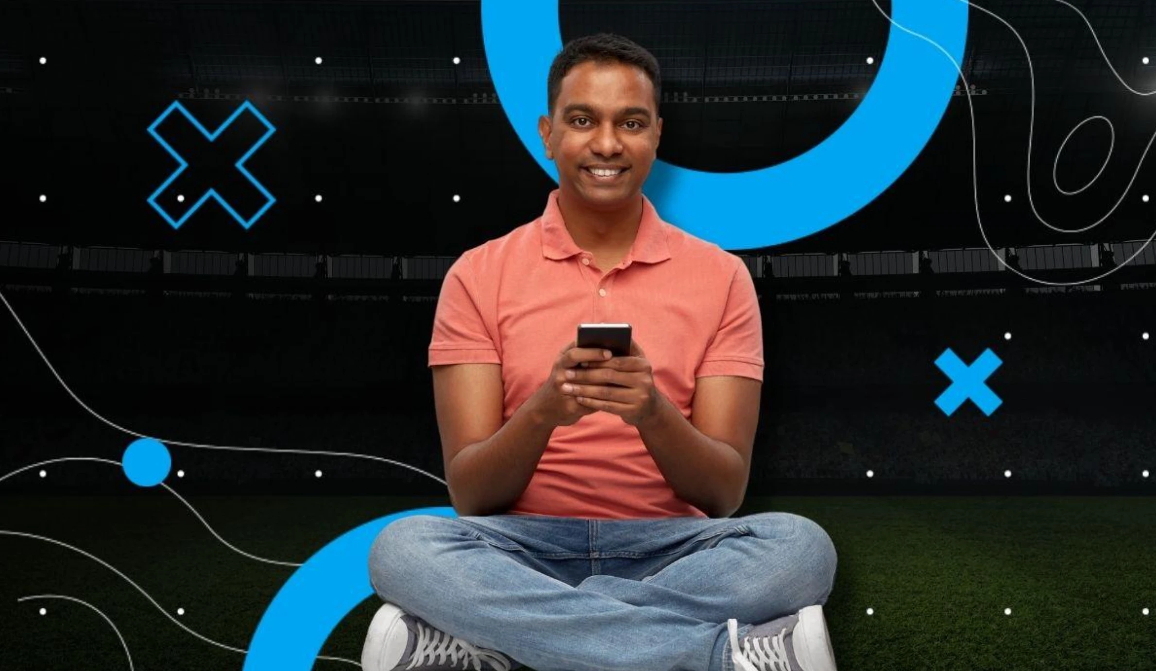 Homem sorrindo com celular em estádio escuro.