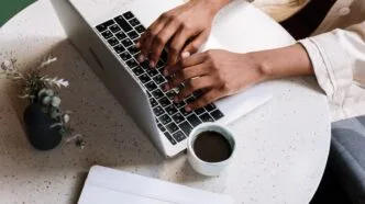 Pessoa digitando em laptop com café ao lado.