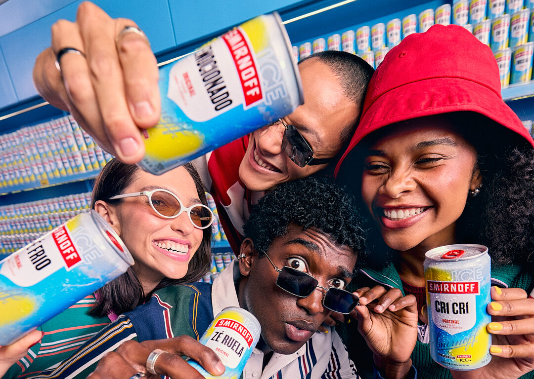 Grupo diverso segura latas de Smirnoff sorrindo.