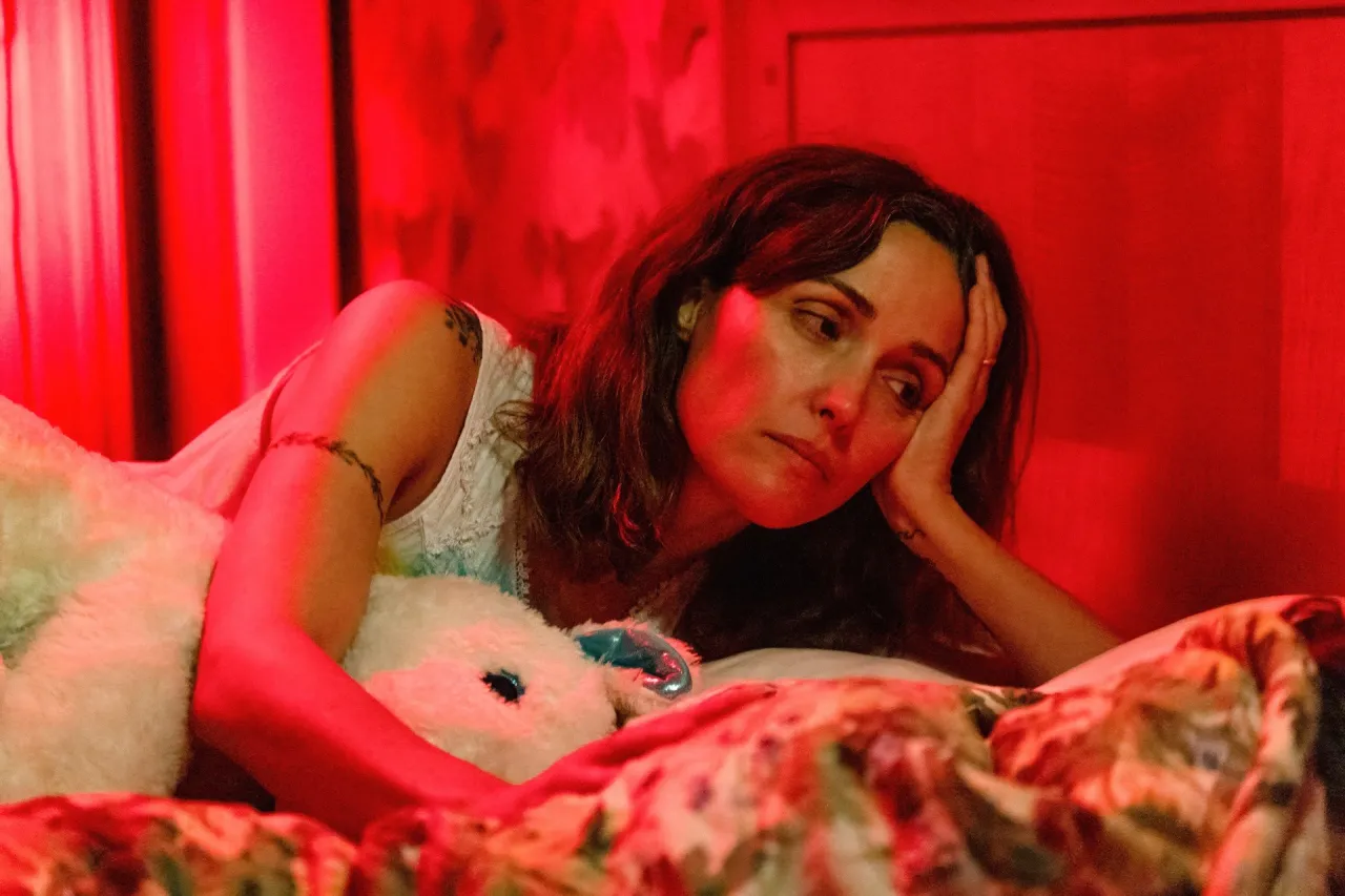 Mulher pensativa em quarto iluminado por luz vermelha.