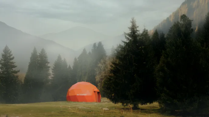 Tenda geodésica laranja em floresta nebulosa