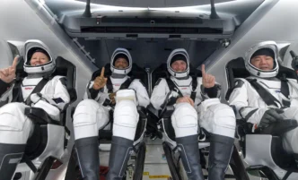 Quatro astronautas em trajes espaciais sorrindo na nave.