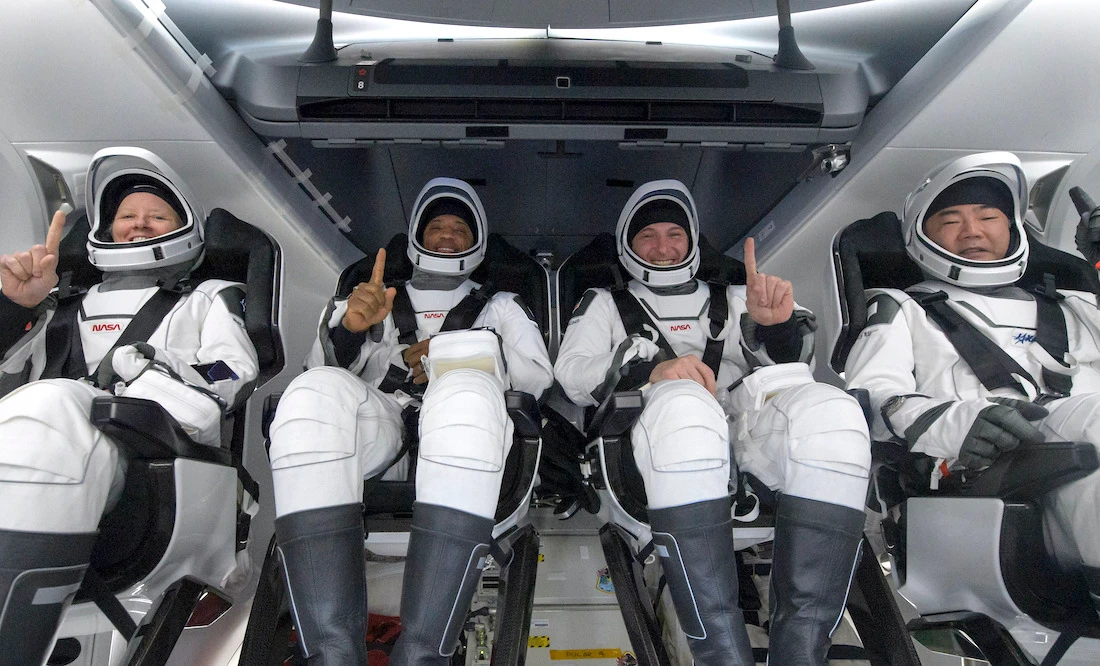 Quatro astronautas em trajes espaciais sorrindo na nave.
