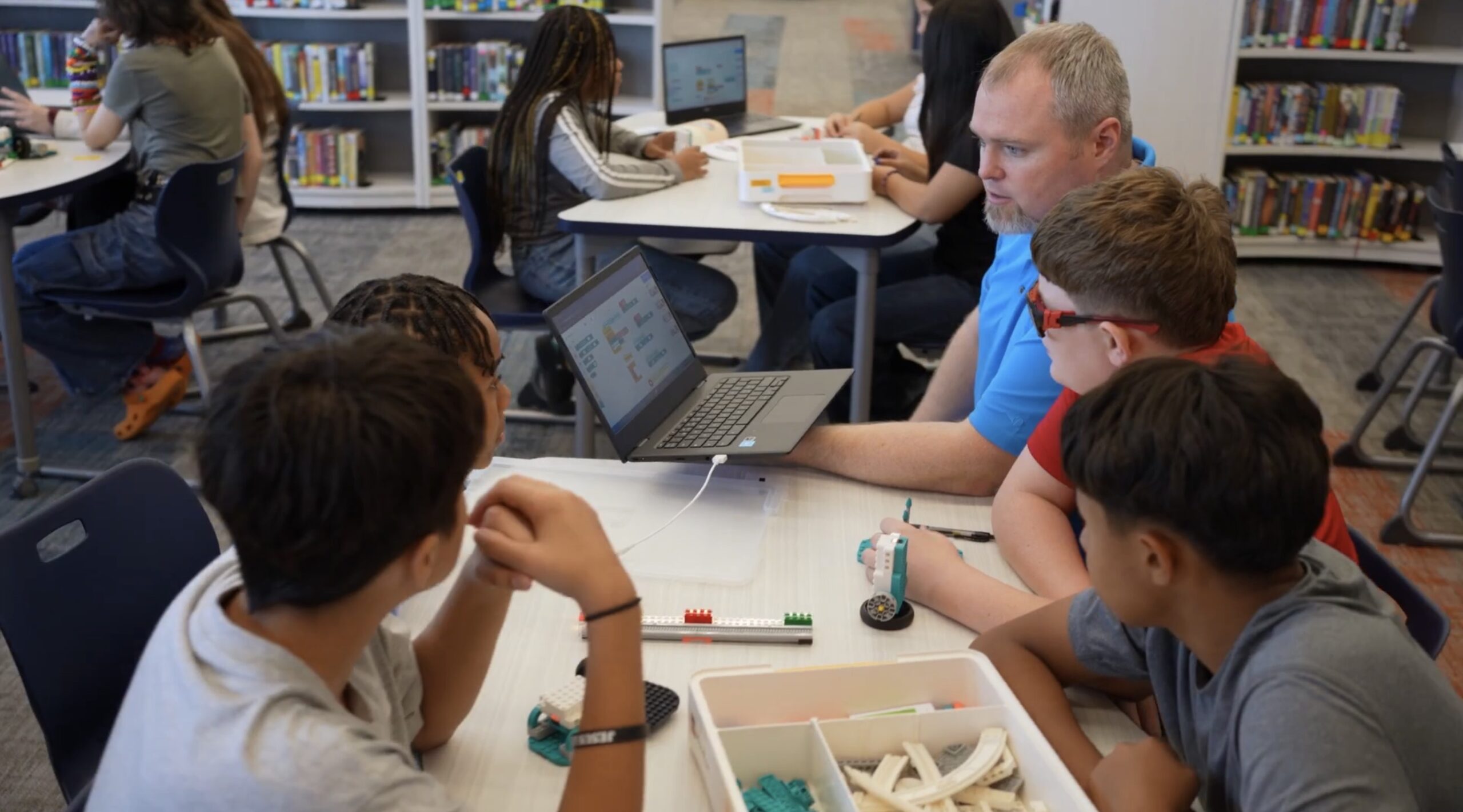 Crianças programando em laptops na biblioteca.