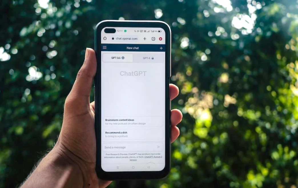 AI-SPM. Smartphone exibindo site ChatGPT em ambiente externo.