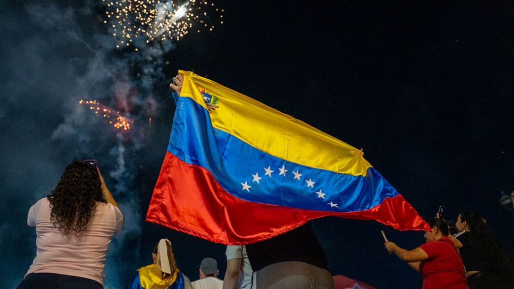 Pessoas celebrando com bandeira da Venezuela e fogos.