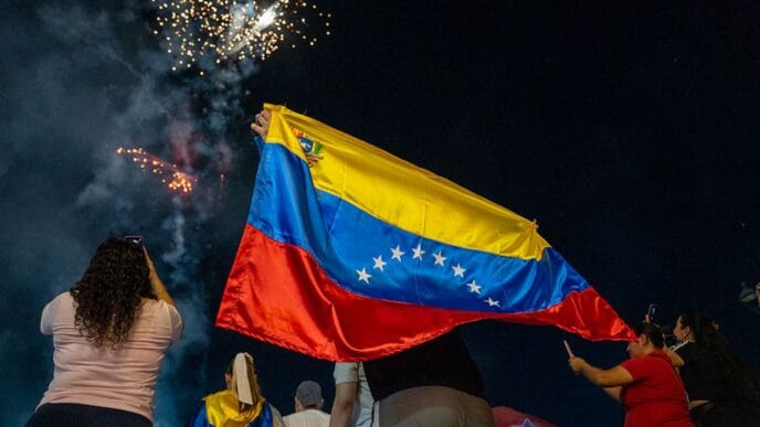 Pessoas celebrando com bandeira da Venezuela e fogos.