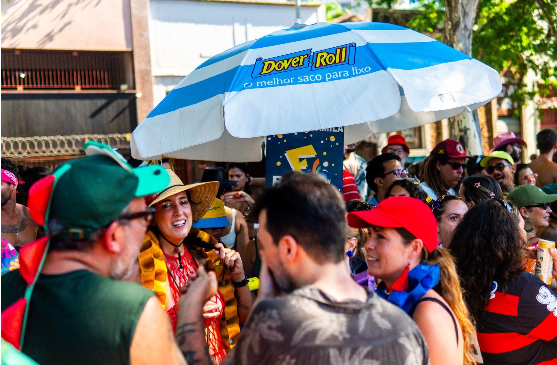 Pessoas fantasiadas sob guarda-sol em evento ao ar livre.