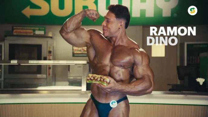 Fisiculturista segurando sanduíche em restaurante.