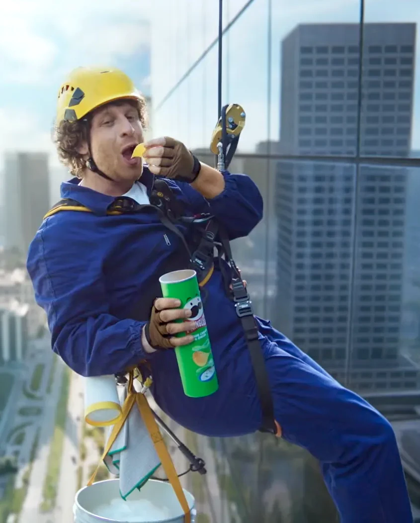 Trabalhador pendurado comendo batata no alto prédio.