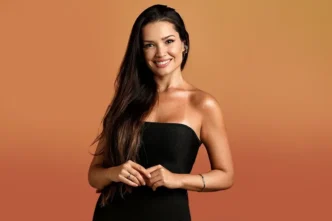 Mulher sorrindo com vestido preto e fundo laranja.