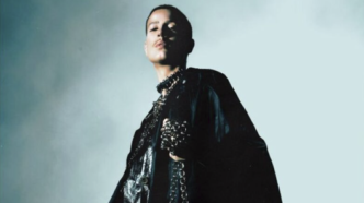 Pessoa em traje preto com colar na penumbra.