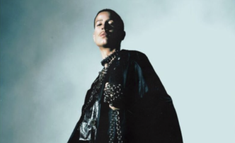 Pessoa em traje preto com colar na penumbra.