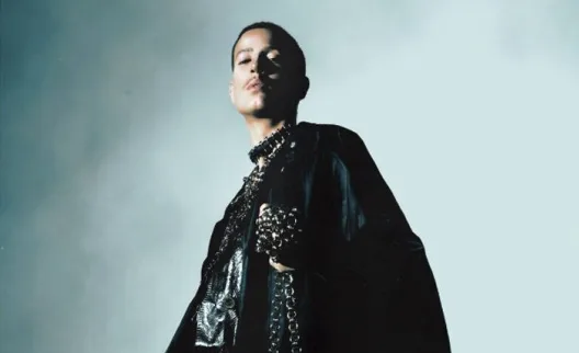 Pessoa em traje preto com colar na penumbra.