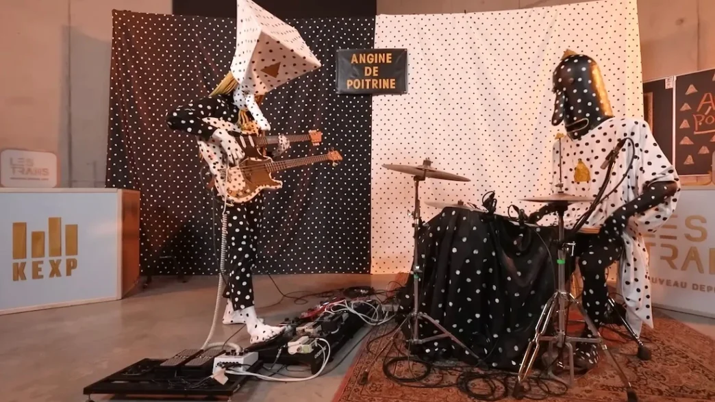 Banda mascarada tocando em estúdio, fundo de bolinhas.