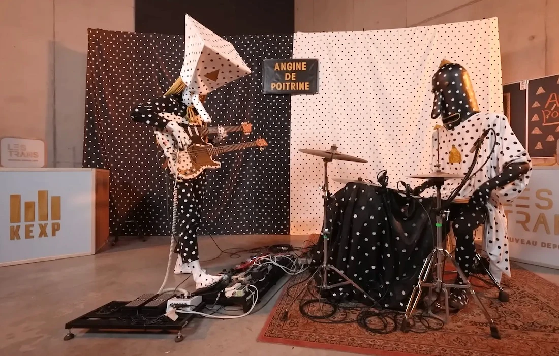 Banda mascarada tocando em estúdio, fundo de bolinhas.