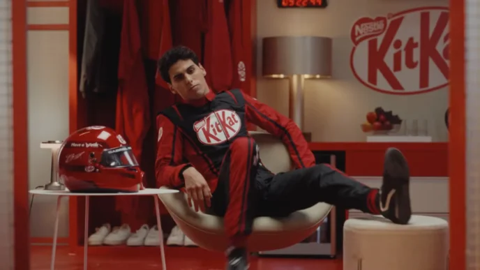 Piloto relaxa em vestiário KitKat, capacete ao lado.