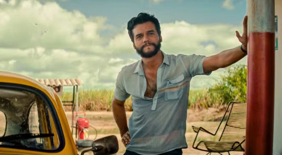 Homem ao lado de carro amarelo em área rural.