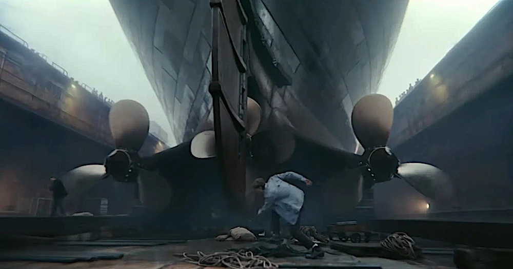 Homem trabalhando sob hélices de navio em construção.