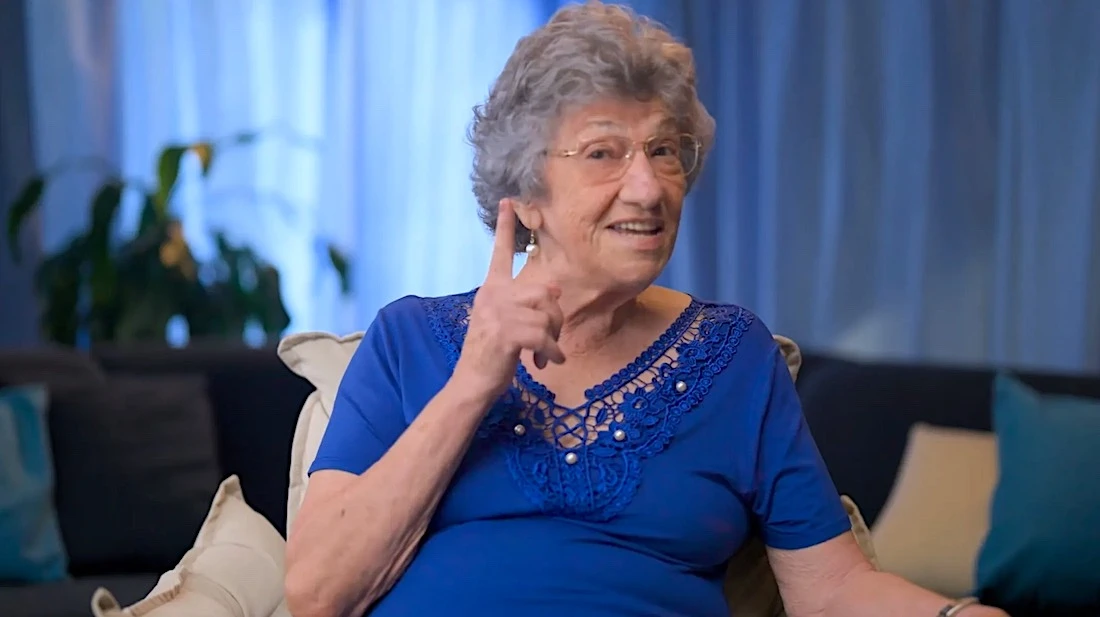 Senhora idosa sorrindo e gesticulando no sofá