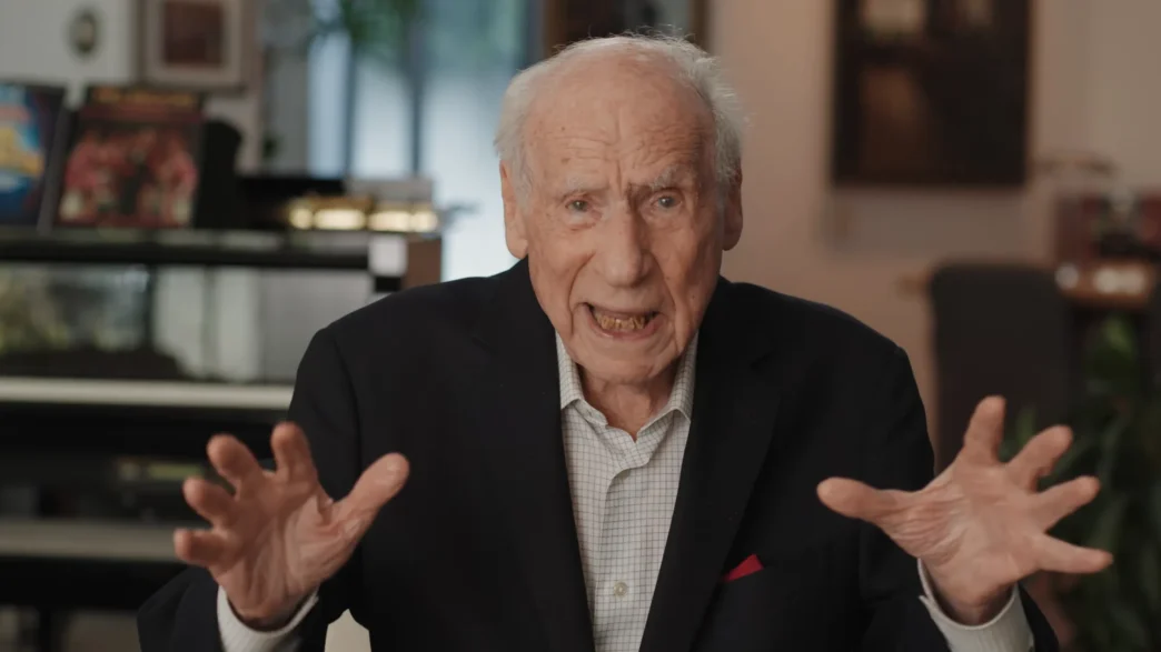 Idoso gesticulando durante entrevista em ambiente interno