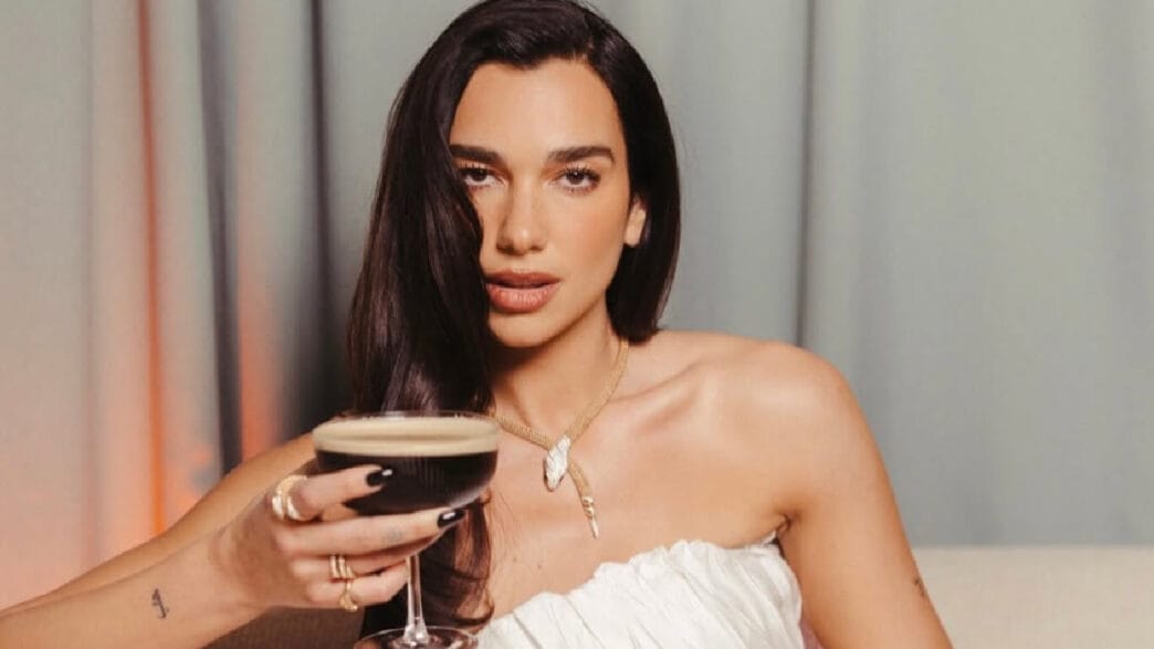 Mulher com vestido branco segurando coquetel escuro