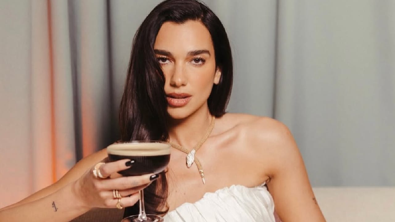 Mulher com vestido branco segurando coquetel escuro