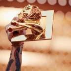 Mão segurando troféu dourado contra luzes desfocadas