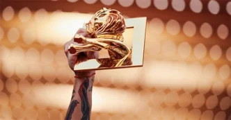 Mão segurando troféu dourado contra luzes desfocadas