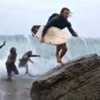 Homem com prancha fugindo de criaturas na praia